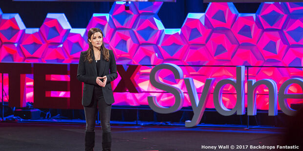 A woman stands on a stage with a TEDxSydney sign in the background, addressing an audience about the modular approach to innovation.