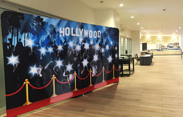Red carpet Hollywood-themed photo backdrop in a hallway with tables, chairs, and Party Drops in the background.