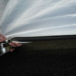 Hands zipping fabric to a metal frame on a dark surface, preparing a scenic backdrop for an upcoming event.